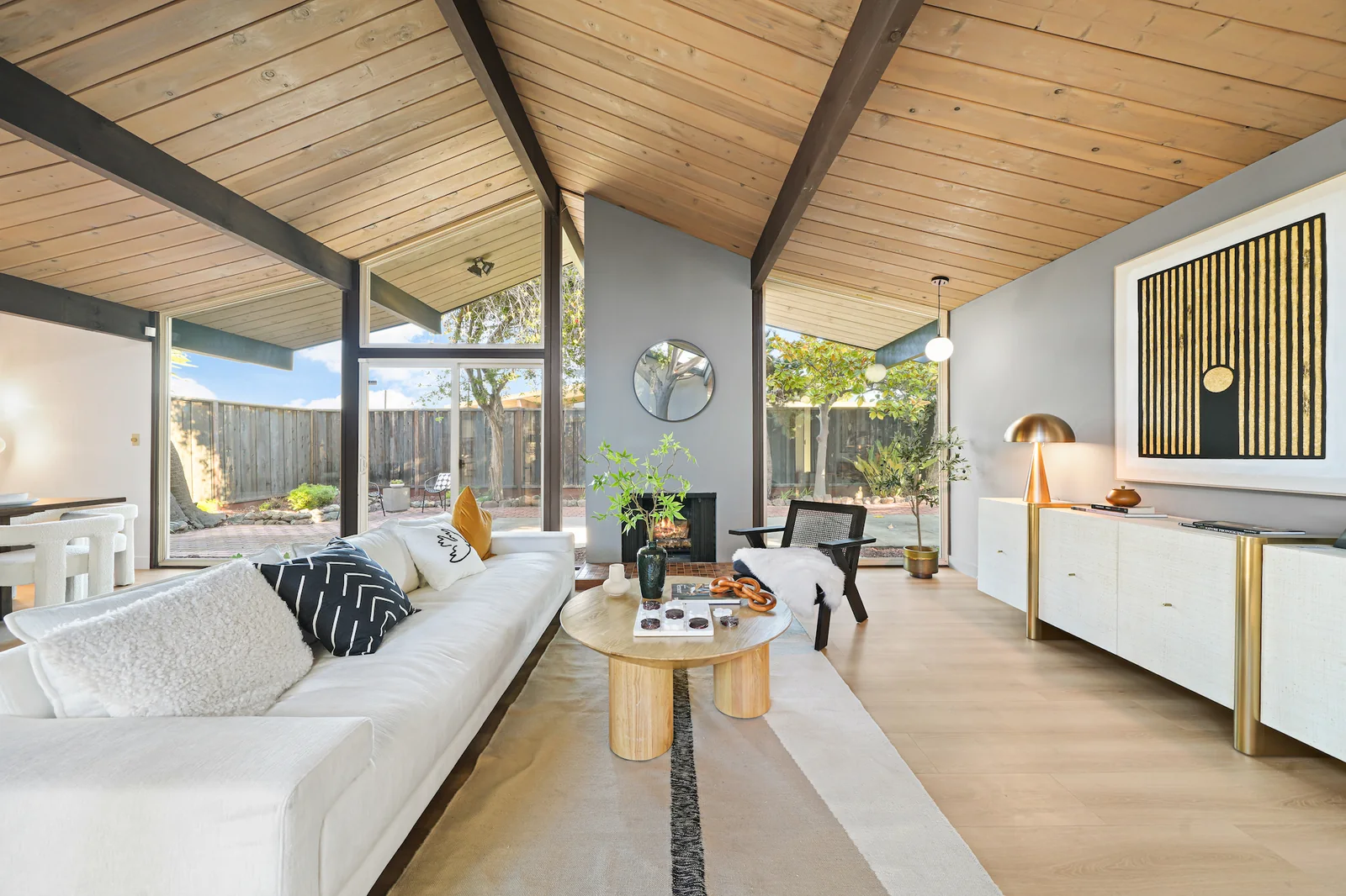 Living room interior showing a vaulted ceiling of wood decking over exposed beams, a wall of glass to a fenced garden, and a free-standing seating area.